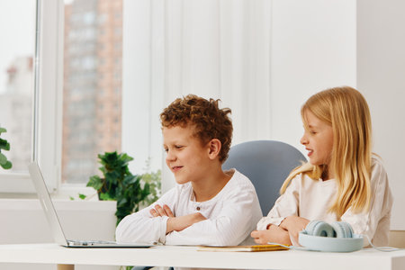 Happy brother and sister studying together at home using laptops for elearning The Caucasian children are sitting at a table in the living room, fully concentrated on their online education They areの写真素材