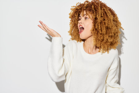 Female with curly hair expressing surprise against a white background, wearing a cozy sweater,...