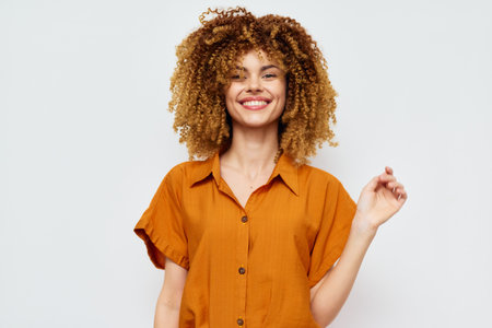 Smiling woman with curly hair in an orange shirt against a light background, showcasing confidence and happiness in a casual setting Perfect for lifestyle or fashion themesの写真素材