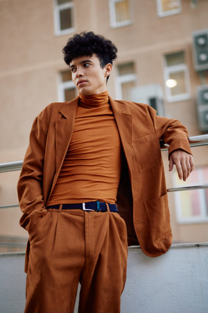 Stylish young man in a brown outfit standing against a modern urban backgroundの写真素材