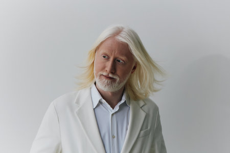 Stylish elderly man with long white hair in a formal white suit against a soft light background,...
