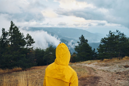 A person in a yellow raincoat standing on a dirt road admiring majestic mountains in the distanceの写真素材