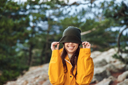 A woman in stylish yellow raincoat and hat covering her eyes while standing on rocky hill...