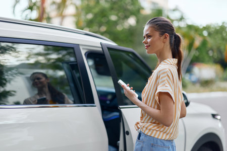 Young woman standing next to a white van with a smartphone in hand, smiling and looking thoughtfully...