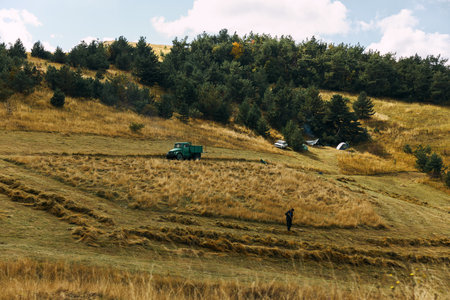 Rural farming landscape with tractor and person standing in field surrounded by nature and wide open spacesの写真素材