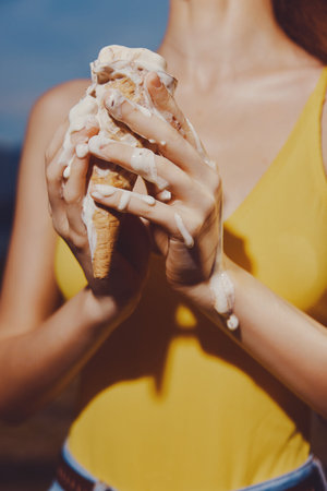 Woman holding a melting ice cream cone in her handsの写真素材