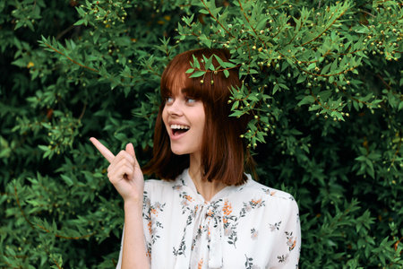 Happy woman pointing towards lush green plants in backgroundの写真素材