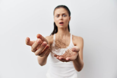 Hair loss, worried woman, shedding hair, hands, emotional expression, health concerns, anxiety about hair, pale background, personal care issues, beauty strugglesの写真素材