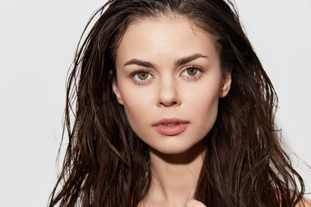 Portrait of a young woman with wet hair against a plain white background, showcasing natural beauty...