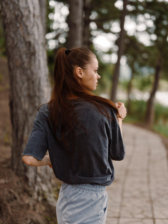 Thoughtful young woman walking along a serene forest path, reflecting on her journey while enjoying...