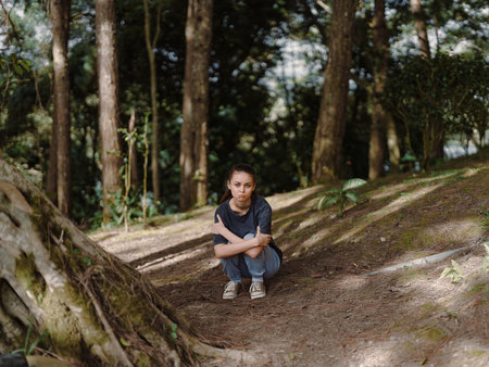 Thoughtful young woman sitting on the forest floor, surrounded by trees, reflecting on nature, in a quiet and peaceful atmosphere Connection with nature conceptの写真素材