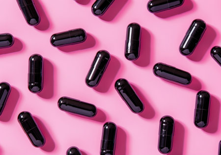 Black capsules scattered on a vibrant pink background, showcasing pharmaceutical or wellness products in a modern and stylish composition Ideal for health, beauty, or supplement themesの素材