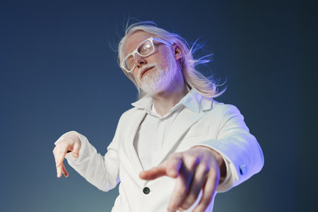 Stylish man with long white hair in a white suit poses confidently against a dark gradient...