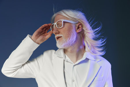 Stylish man with long white hair and glasses in a modern fashion pose, wearing a white suit against...