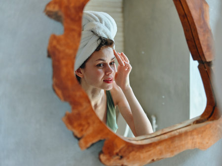 Woman with towel on head admiring reflection in bathroom mirror after washing hairの写真素材