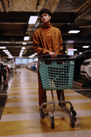 Stylish man in a brown suit standing with a shopping cart in a parking garageの写真素材