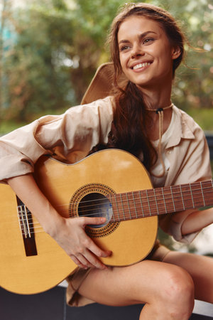 A woman is holding an acoustic guitar and posing for the camera while sitting on a benchの写真素材