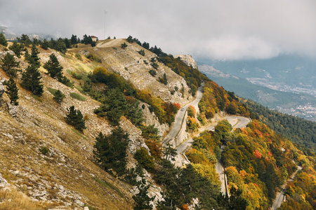 A scenic winding road through the mountains with trees, clouds, and nature views for travel and adventure conceptの写真素材