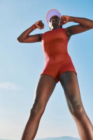 Athletic woman stretching in a red swimsuit against a clear blue skyの写真素材
