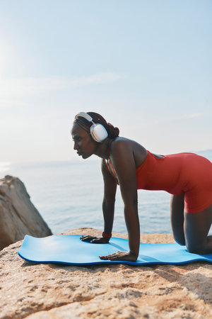 Yoga practice by the ocean with a serene view, featuring a woman in a red outfit on a blue matの写真素材