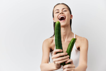 Happy young woman holding cucumbers, smiling joyfully Fresh vegetables, healthy lifestyle, natural beauty, organic food Bright white background enhances the cheerful moodの写真素材