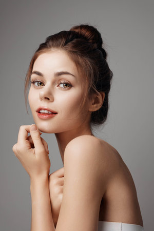 Young woman with hands on face looking at camera on grey backgroundの写真素材