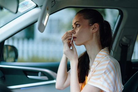 Woman applying makeup in a car interior with natural light, showcasing beauty routine, orange and white striped shirt, beautifully lit environment, modern lifestyleの写真素材