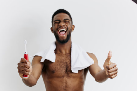 Shirtless man enthusiastically promoting dental hygiene with a toothbrush and thumbs up gesture in a bright settingの写真素材