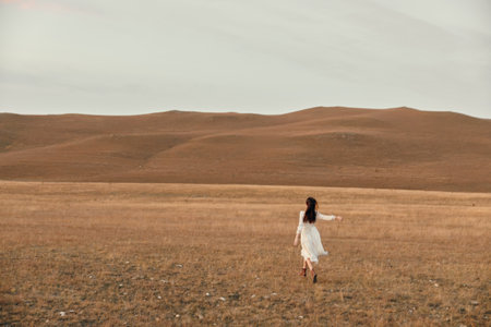 Woman walking through scenic open field with hills in background serene nature walk among rolling hillsの写真素材