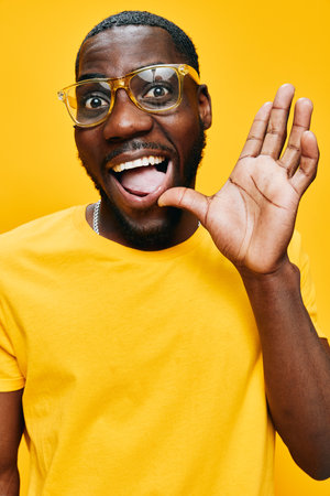 Happy man waving in vibrant yellow t shirt with glasses, expressing joy against a bright yellow background, showcasing enthusiasm and positivity in a cheerful settingの写真素材