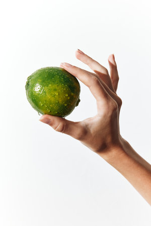 Person holding a green lime in their hand, with a white backgroundの写真素材