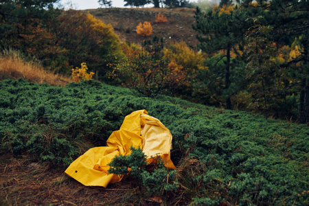 Vibrant yellow raincoat left in serene field with lush trees in background, symbolizing nature and...