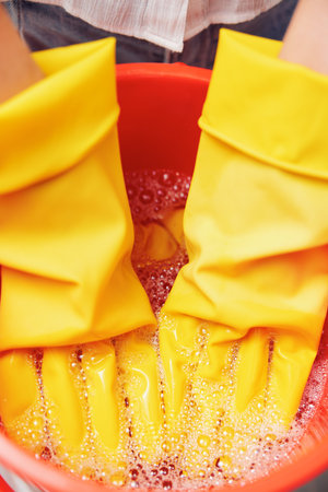 Woman in yellow gloves washing hands in soapy water with sponge in backgroundの写真素材