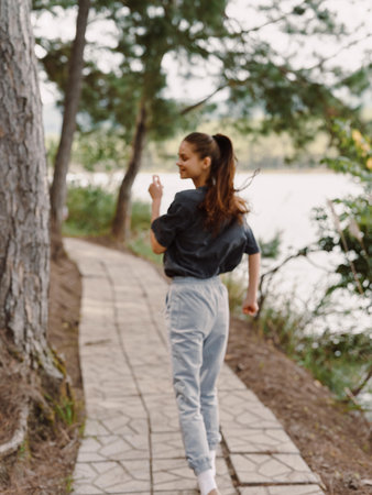 Young woman jogging along a scenic pathway in nature, enjoying an active lifestyle and fitness...