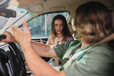 Young couple arguing inside a car, expressing frustration and emotions, natural light illuminating the sceneの写真素材