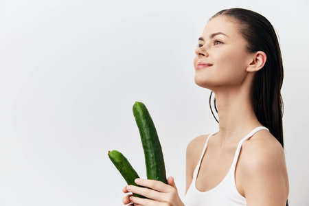 Woman holding cucumbers, smiling with a fresh and healthy expression Minimalistic white background, showcasing natural beauty and wellness concept Ideal for health and lifestyle themesの写真素材
