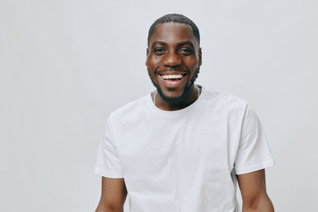 Happy smiling young man wearing a plain white t shirt against a light gray background, expressing...