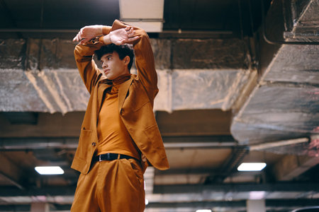 Stylish young man in brown suit stretching in urban settingの写真素材