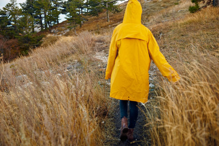 Exploring the Beauty of Nature Person in Yellow Raincoat Walking Through Tall Grass on Hillside with...