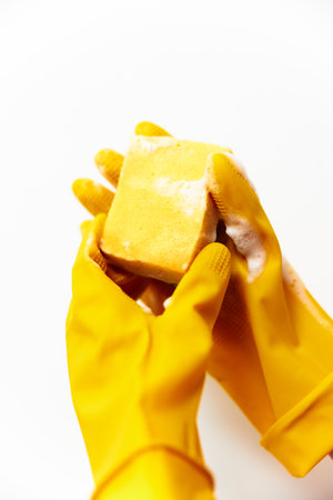 Person in yellow rubber gloves holding soap and sponge on white backgroundの写真素材