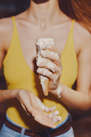 Woman holding melting ice cream cone with yellow top in a casual setting