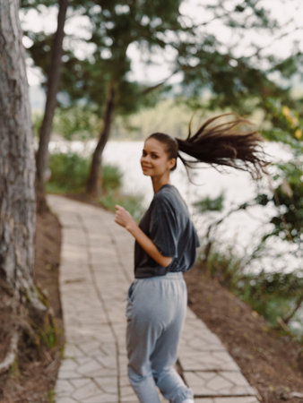 Smiling young woman jogging along a scenic pathway by the water, enjoying an active lifestyle surrounded by nature Health and fitness conceptの写真素材