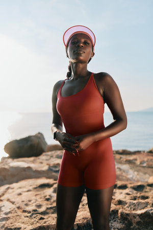 Confident young woman in a red athletic outfit at the beach during sunsetの写真素材