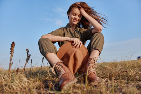Woman enjoying nature in stylish hat and boots sitting in field on travel adventure beauty in the...