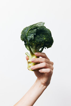 Person holding a piece of broccoli on a white backgroundの写真素材