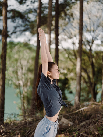 Relaxed young woman practicing yoga outdoors in a serene forest, enjoying the fresh air and connecting with nature Wellness and mindfulness conceptの写真素材