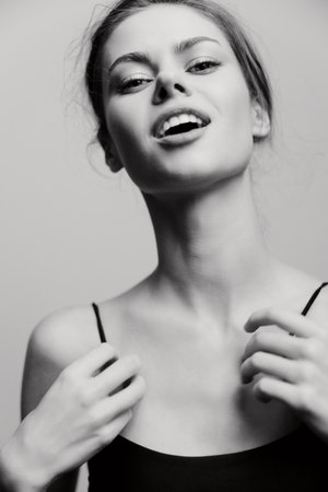 Confident young woman in simple black top, expressing joy and self-assurance. Bright, spirited mood against a soft gray background. Portrait and beauty concept.の写真素材