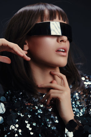 Futuristic glasses, sequinned dress, woman with hand on face, head tilted to side, stylish and modern appearance, capturing an avantgarde, fashionforward aestheticの写真素材