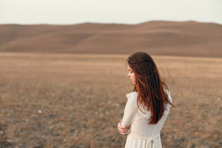 Woman in white dress standing in open field with mountain landscape in background serene travel beauty in nature conceptの写真素材