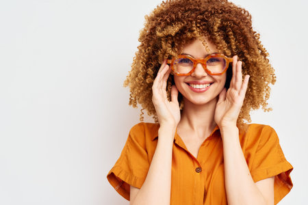 smiling woman with curly hair wearing orange glasses and stylish outfit against a light background, joyful expression, concept of fashion and confidenceの写真素材